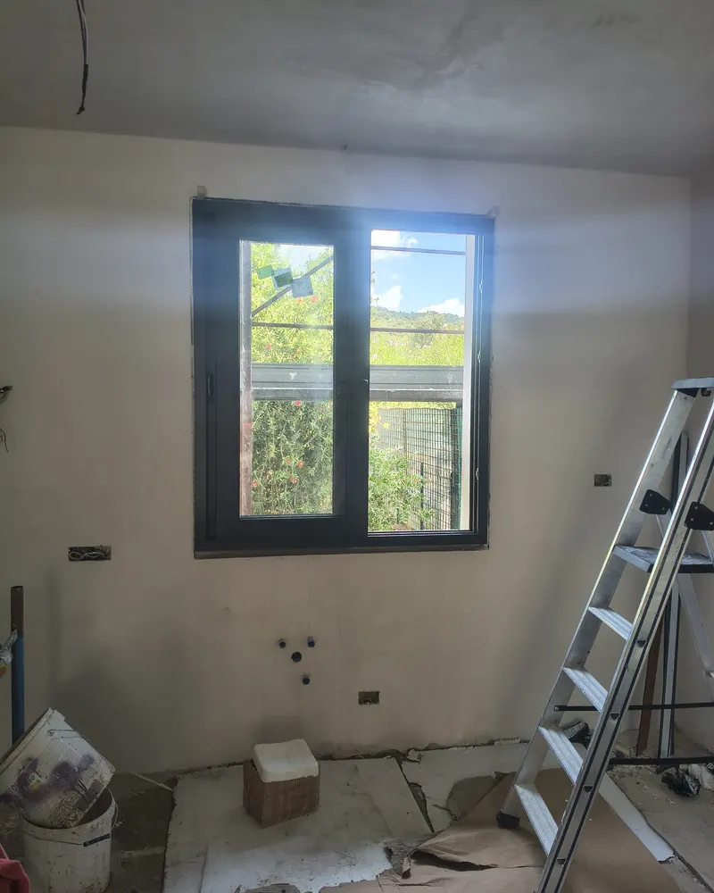 Finestra a due ante in PVC grigio antracite vista dall’interno di una stanza intonacata