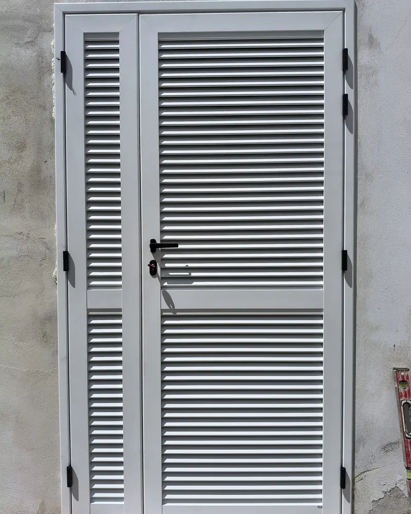 Persiana in alluminio a due ante, colore grigio chiaro, appoggiata al muro prima del montaggio